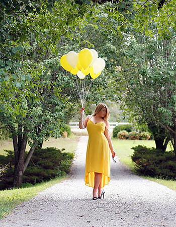 Lexy Jorden of Minneapolis, MN Minneapolis escort Lexy Jorden standing on a gravel road wearing a yellow dress and holding yellow ballons